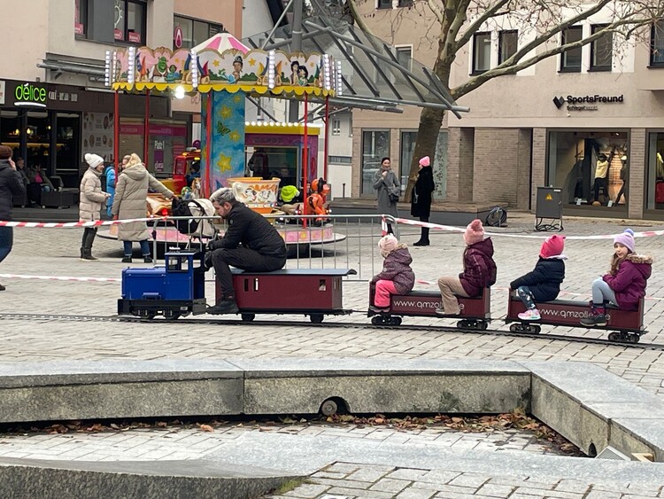 Mobile 5-Zoll-Bahn mit blauer Lok und roten Waggons im Einsatz bei einem Event, umgeben von Kindern und Familien. Perfekt für buchbare Veranstaltungen von QMZoller Amusement UG. Mobile 5-Zoll-Bahn mit blauer Lok und roten Waggons im Einsatz bei einem Event, umgeben von Kindern und Familien. Perfekt für buchbare Veranstaltungen von QMZoller Amusement UG.